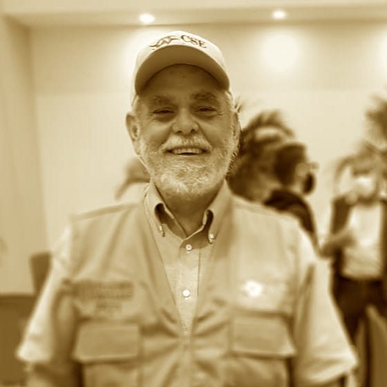 Sepia photograph: Tom Loudon, bearded and in a cap and field vest, smiles at the camera indoors.