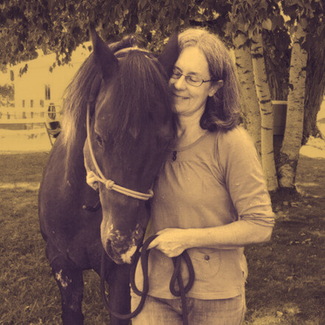 Sepia photograph: Jenny Atlee stands under a birch tree beside a dark horse in a halter, holding the lead rope, looking down at the horse and smiling.